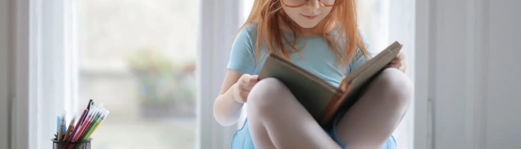 戴眼鏡的女孩盤腿坐在窗邊專注看書，呼應兒童智力評估